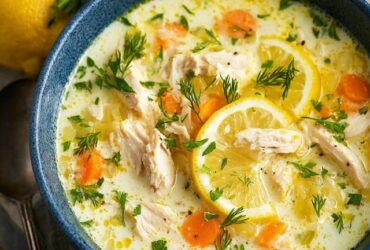 Lemon chicken soup in a white bowl with shredded chicken, orzo pasta, silky lemon-egg broth, lemon slices, fresh dill garnish, golden surface from emulsified egg