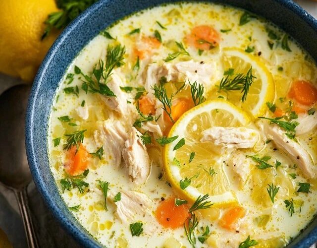 Lemon chicken soup in a white bowl with shredded chicken, orzo pasta, silky lemon-egg broth, lemon slices, fresh dill garnish, golden surface from emulsified egg