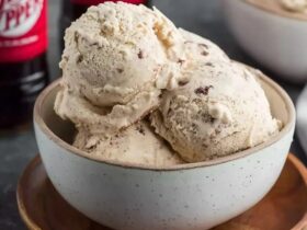 Dr Pepper ice cream scooped into a waffle cone with creamy beige-pink color, soda-reduction swirl visible, drip on side, cherry on top, dark soda in glass behind