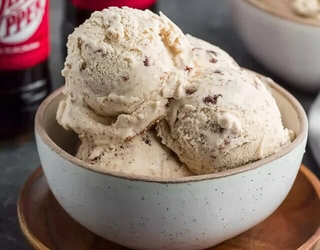 Dr Pepper ice cream scooped into a waffle cone with creamy beige-pink color, soda-reduction swirl visible, drip on side, cherry on top, dark soda in glass behind