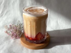 Strawberry iced milk tea in a tall glass with bright pink strawberry puree at the bottom, creamy milk gradient, ice cubes, tea straw, fresh strawberries on rim