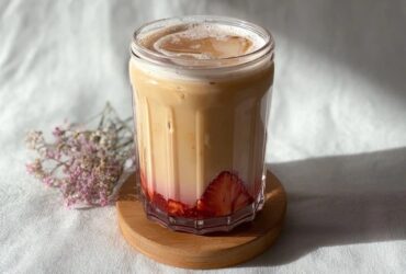 Strawberry iced milk tea in a tall glass with bright pink strawberry puree at the bottom, creamy milk gradient, ice cubes, tea straw, fresh strawberries on rim