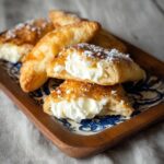 Cream cheese puff pastries on a baking sheet with golden flaky squares, sweetened cream cheese filling in center, dusting of powdered sugar, raspberry on top