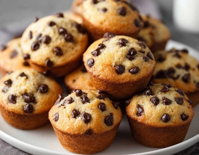 Chocolate chip muffins on a wire rack with tall domed golden tops, chocolate chips peeking through cracks, paper liners, soft tender crumb visible at edge
