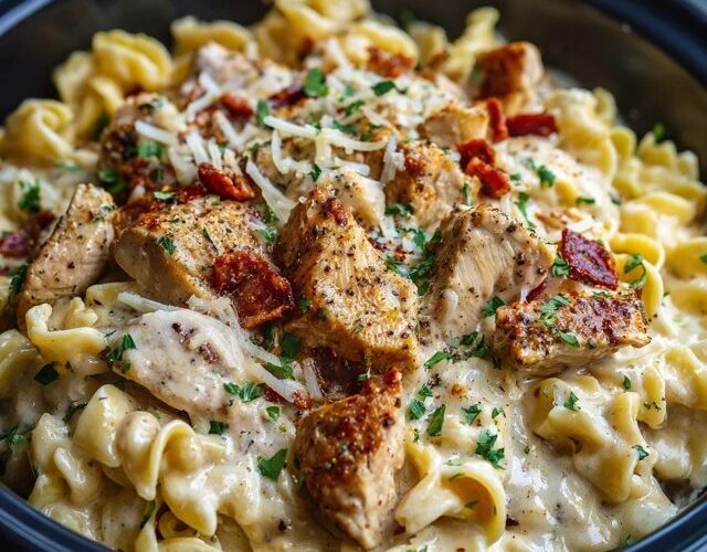 Chicken alfredo pasta on a white plate with creamy white sauce coating fettuccine ribbons, golden sliced grilled chicken on top, fresh parsley, parmesan shavings, black pepper