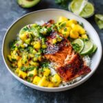Mango salsa salmon bowl with crispy-skinned pan-seared salmon over white rice, bright orange mango salsa with red bell pepper, avocado slices, lime wedges, fresh cilantro