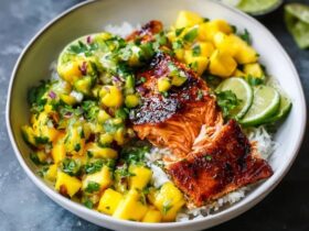 Mango salsa salmon bowl with crispy-skinned pan-seared salmon over white rice, bright orange mango salsa with red bell pepper, avocado slices, lime wedges, fresh cilantro