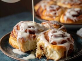 Cinnamon rolls with cream cheese icing in a baking dish, tall pillowy soft rolls with cinnamon-sugar swirls visible, thick white cream cheese glaze melting over warm tops, one roll lifted