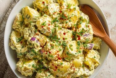 Classic potato salad in a white serving bowl, tender chunks of waxy potato coated in creamy dressing, diced hard-boiled egg, celery, dill pickle, red onion, fresh dill, paprika dusting
