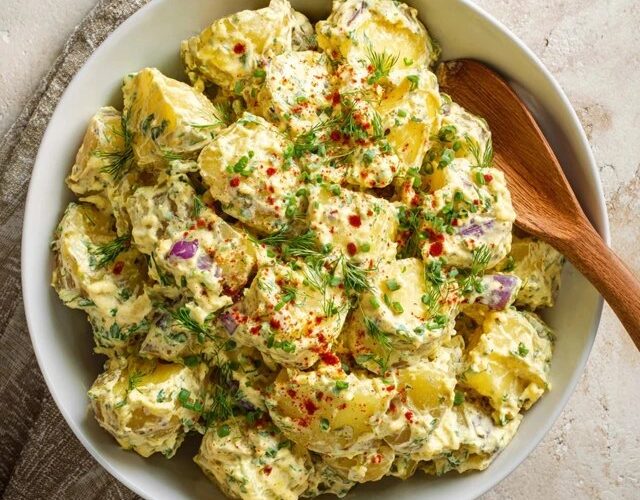 Classic potato salad in a white serving bowl, tender chunks of waxy potato coated in creamy dressing, diced hard-boiled egg, celery, dill pickle, red onion, fresh dill, paprika dusting