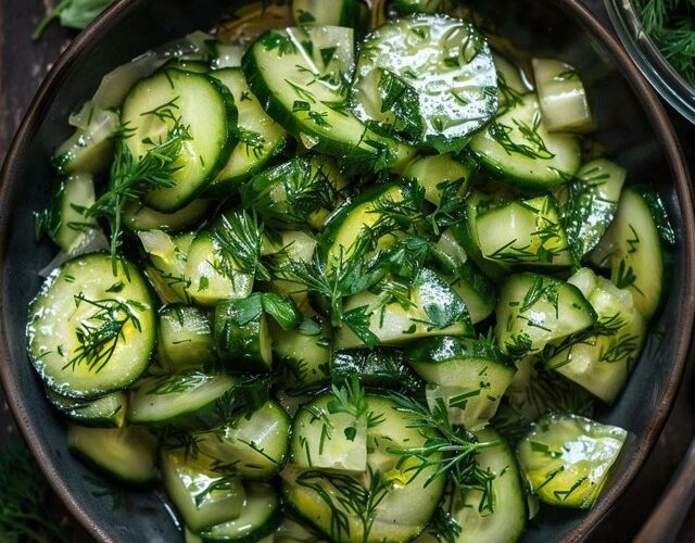 Cucumber dill salad in a white bowl, thin-sliced cucumber rounds tossed with creamy sour cream dressing, red onion slivers, plenty of fresh chopped dill, cracked black pepper, served on a wooden board