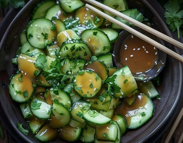 Asian smashed cucumber salad in a black bowl, chunky cucumber pieces with jagged edges glistening with sesame oil and soy sauce, minced garlic, toasted sesame seeds, red chili flakes, sliced scallions on top