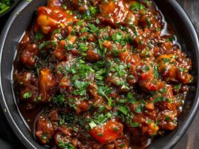 Vegetable manchurian gravy in a black bowl, golden-fried vegetable balls floating in glossy dark-red gravy with onion bell pepper specks, scallion garnish, fried rice in a small bowl beside