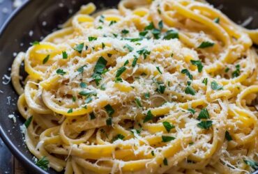 Linguine aglio e olio on a white pasta plate, glossy strands coated in olive oil with thinly sliced golden garlic chips, red pepper flake specks, fresh chopped parsley, grated parmesan, served with a fork twirling pasta