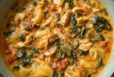 Creamy chicken tortellini soup in a white bowl, golden cream-colored broth filled with plump cheese tortellini, shredded chicken pieces, wilted green spinach leaves, diced carrots, parmesan sprinkled on top, crusty bread on the side