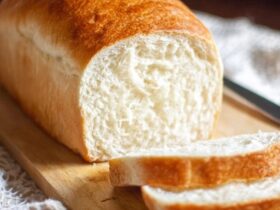 White sandwich bread sliced on a wooden cutting board, golden-brown crust with pillowy soft white interior, even uniform crumb structure visible in cut slices, butter dish and knife beside, kitchen towel underneath