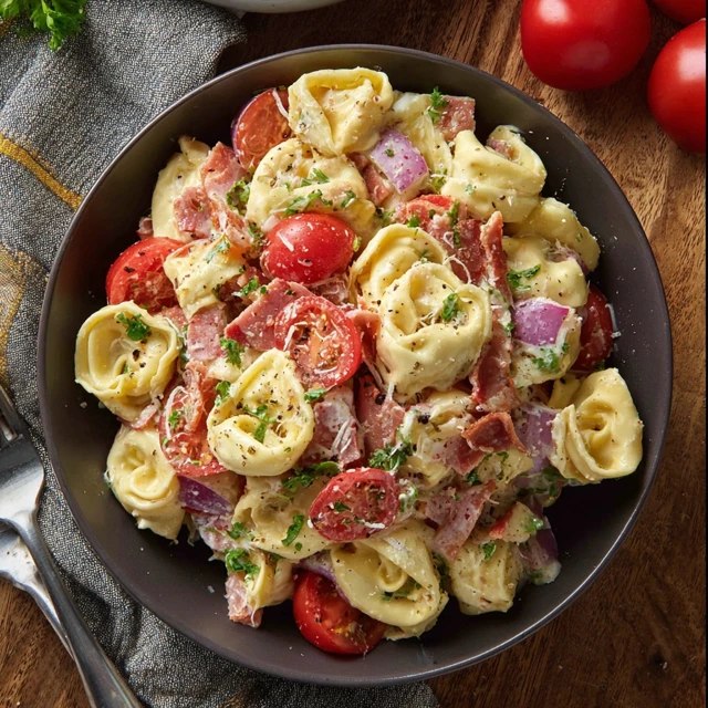 Tortellini salad with bacon in a large white serving bowl, plump cheese tortellini tossed with crispy bacon pieces, fresh baby spinach leaves, halved cherry tomatoes, sliced red onion, shredded parmesan, glossy Italian vinaigrette dressing coating everything, fresh basil leaves on top