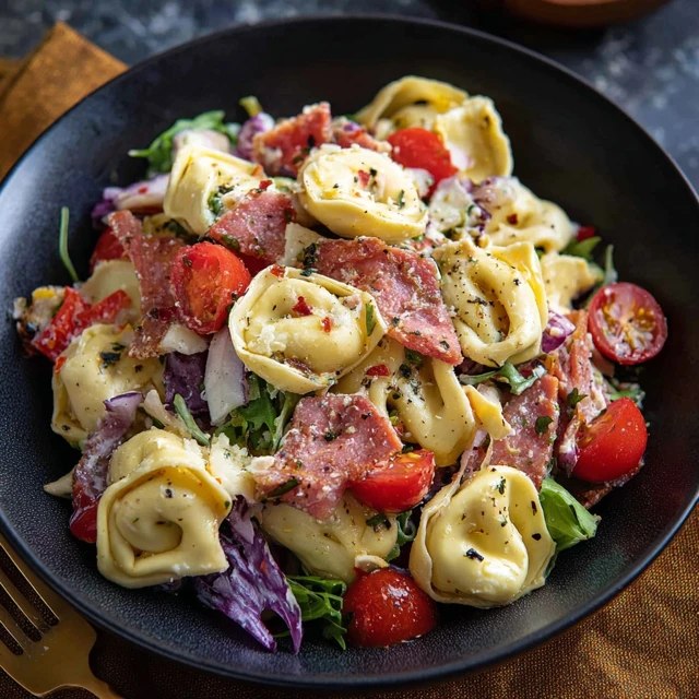 Close-up of tortellini salad showing pillowy cheese-filled tortellini coated in Italian dressing, smoky bacon crumbles, vibrant green spinach, bright red cherry tomato halves, white parmesan curls, finely chopped basil