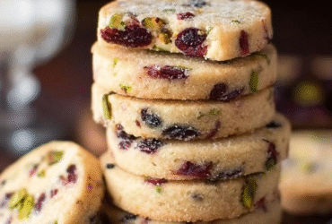 Cranberry pistachio shortbread cookies on a wire rack, pale buttery shortbread rounds with ruby-red dried cranberries and bright green chopped pistachios embedded throughout, festive holiday cookie tin in background
