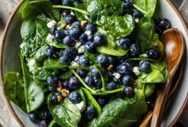 Spinach blueberry salad in a wooden bowl, fresh baby spinach leaves with vibrant blue blueberries scattered throughout, crumbled white feta cheese chunks, golden toasted pecans, drizzled with light lemon vinaigrette
