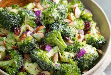 Broccoli salad with almonds in a large white serving bowl, bright green raw broccoli florets coated in creamy ivory dressing, crispy crumbled bacon bits, ruby red cranberries, golden toasted almond slivers, red onion specks