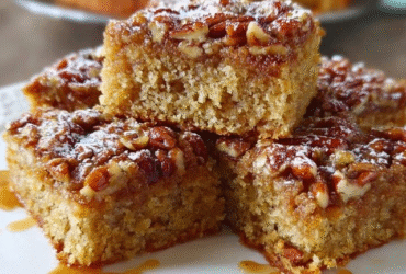 Pecan pie bars cut into squares on parchment paper, dark amber sticky pecan topping covering shortbread base, whole pecan halves arranged on top, glossy caramelized surface, square portion bites visible