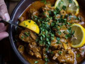 Chicken curry with lemon in a Dutch oven, golden yellow coconut curry sauce coating tender chicken pieces, bright lemon slices floating on top, fresh cilantro garnish, steamed basmati rice on the side, lime wedges