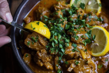 Chicken curry with lemon in a Dutch oven, golden yellow coconut curry sauce coating tender chicken pieces, bright lemon slices floating on top, fresh cilantro garnish, steamed basmati rice on the side, lime wedges