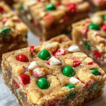 Holiday cookie bars cut into squares on parchment paper, soft buttery sugar cookie base with thick swirly cream cheese frosting layer on top, colorful red green and white festive sprinkles covering everything, cookie tin with more bars beside