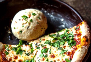 Classic homemade pizza overhead, golden crispy crust with charred bubbles, glossy red tomato sauce, melted bubbly mozzarella, fresh basil leaves scattered on top, dish fills the frame