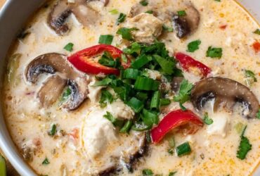 Slow cooker tom kha gai soup in a deep bowl, creamy coconut broth, tender chicken pieces, mushrooms, fresh cilantro and Thai chili, lime wedge on the rim, soft natural light