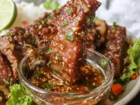 Crying tiger beef sliced on a wooden cutting board, charred edges, deep pink medium-rare interior, served with small bowl of nam jim jaew dipping sauce, fresh cilantro and sticky rice on the side