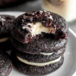 Black velvet cheesecake cookies on a black slate board, jet black cocoa cookies with white cream cheese centers oozing slightly, dramatic moody lighting, perfect for Halloween