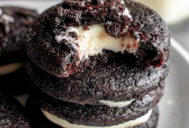 Black velvet cheesecake cookies on a black slate board, jet black cocoa cookies with white cream cheese centers oozing slightly, dramatic moody lighting, perfect for Halloween