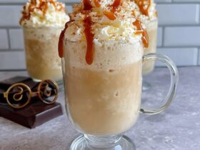 Two tall mugs of frozen butterbeer slush with thick foamy butterscotch whipped topping overflowing, dripping butterscotch drizzle down the sides, magical autumn light, Harry Potter themed