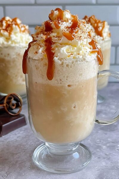Two tall mugs of frozen butterbeer slush with thick foamy butterscotch whipped topping overflowing, dripping butterscotch drizzle down the sides, magical autumn light, Harry Potter themed