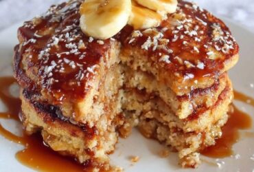 Stack of fluffy oatmeal pancakes on a wooden plate, golden brown edges, pat of butter melting on top, drizzle of maple syrup running down the sides, fresh blueberries scattered around, bright morning light