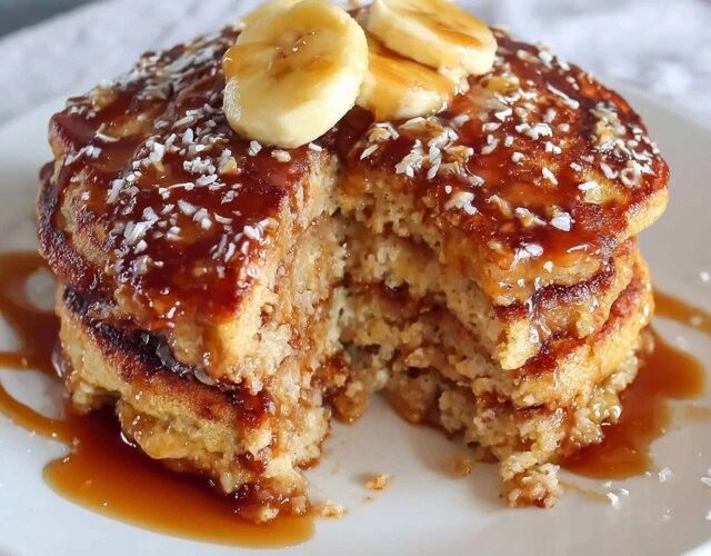 Stack of fluffy oatmeal pancakes on a wooden plate, golden brown edges, pat of butter melting on top, drizzle of maple syrup running down the sides, fresh blueberries scattered around, bright morning light