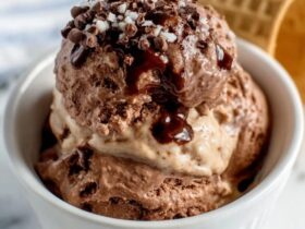Two scoops of homemade chocolate ice cream in a glass coupe, glossy dark chocolate surface, slight melt drip showing creamy interior, chocolate sauce drizzle and chocolate shavings on top
