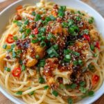 Singapore black pepper cauliflower with spaghetti in a deep bowl, crispy golden cauliflower florets coated in glossy dark pepper sauce, twirled spaghetti, green onion garnish, sesame seeds, moody dramatic lighting