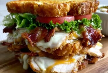 Crispy ultimate club sandwich cut diagonally and held together with frilly toothpicks, three layers of toasted bread, layers of crispy bacon, sliced turkey, lettuce, tomato, avocado, fanned out on a wooden board with potato chips and a pickle spear