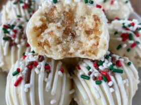 Sugar cookie truffles arranged on a white plate, white chocolate coated balls with red and green sprinkles, festive holiday styling, snowflake doily underneath