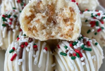 Sugar cookie truffles arranged on a white plate, white chocolate coated balls with red and green sprinkles, festive holiday styling, snowflake doily underneath