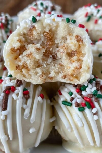 Sugar cookie truffles arranged on a white plate, white chocolate coated balls with red and green sprinkles, festive holiday styling, snowflake doily underneath