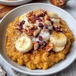Pumpkin oatmeal bowl in a ceramic bowl, creamy orange oats topped with toasted pecans, drizzle of maple syrup, cinnamon dust, dollop of Greek yogurt, fresh pomegranate seeds, warm autumn light