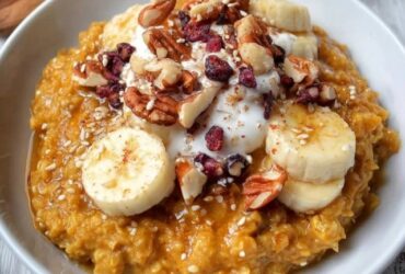 Pumpkin oatmeal bowl in a ceramic bowl, creamy orange oats topped with toasted pecans, drizzle of maple syrup, cinnamon dust, dollop of Greek yogurt, fresh pomegranate seeds, warm autumn light