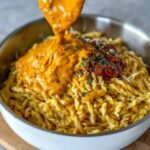 Creamy macaroni and cheese in a wide pan, glossy orange cheese sauce coating elbow pasta, pulled cheese strands when spoon lifts, cracked black pepper and fresh chives on top