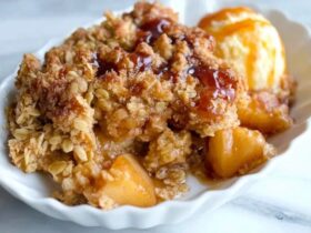 Apple crisp in a baking dish with golden bubbly streusel topping over cinnamon apples, scoop of vanilla ice cream melting on top, caramel drizzle, fall light