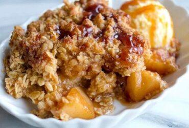 Apple crisp in a baking dish with golden bubbly streusel topping over cinnamon apples, scoop of vanilla ice cream melting on top, caramel drizzle, fall light