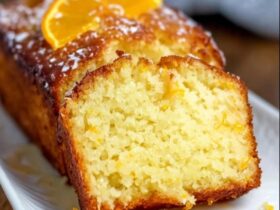 Orange glaze pound cake on a wire rack with white glaze drizzled down the sides, golden buttery loaf cake with tight crumb, fresh orange zest on top, slice cut showing moist interior